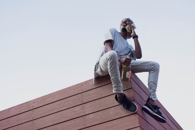 男子坐在屋顶上，手里拿着电话和瓶子